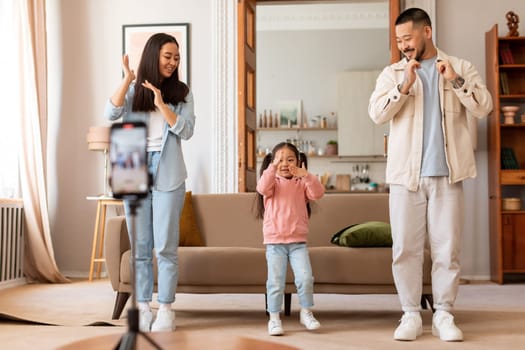 Asian influencers with daughter shooting dance video on phone indoor