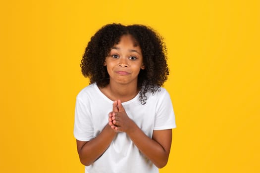 Cheerful funny curly teen black schoolgirl in white t-shirt praying, asking for miracle