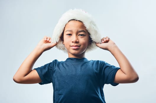 The coolest holiday of them all. Studio shot of a cute little boy wearing a Santa hat against a grey background.