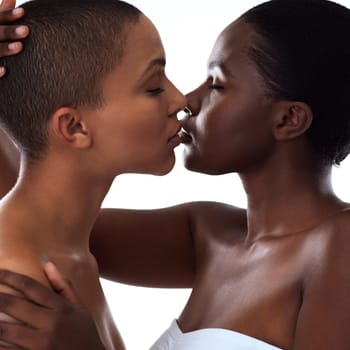The kiss says a lot. Studio shot of two beautiful young women holding each other while going in for a kiss and standing against a white background.