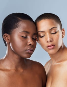 Close your eyes and listen to your heart. Portrait of two beautiful young women standing close to each other with their eyes closed against a grey background.