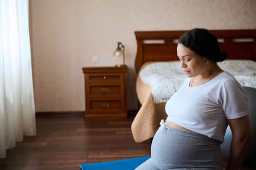 Portrait of a middle aged pregnant woman swith big belly in pregnancy trimester third, exercising on yoga mat at home