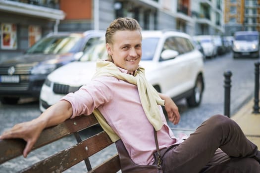 Happy and handsome individual with lazy and carefree expression, smiling while sitting on bench in urban city. Person's relaxed demeanor reflects their contentment and enjoyment in moment.