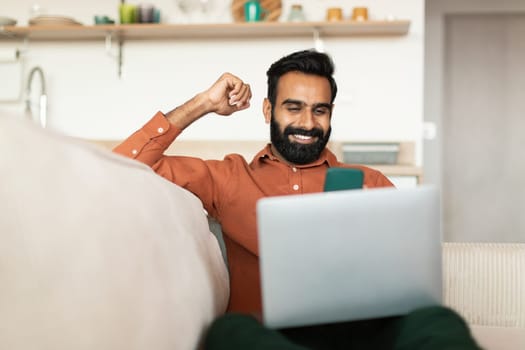 Happy arabic man with laptop celebrating, gesturing yes sitting indoor