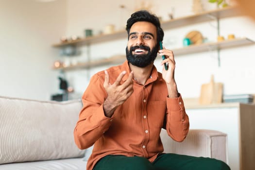 Smiling Arab Guy Talking On Cellphone Enjoying Communication At Home