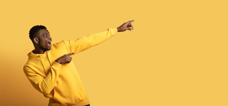 Excited african american guy showing empty space on yellow