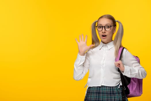 world book day surprised schoolgirl blonde with ponytails pink backpack on yellow background