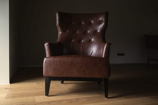 Brown leather armchair in an empty dark room by the window