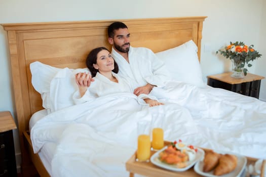 Couple Hugging In Comfortable Bed With Breakfast Tray At Hotel
