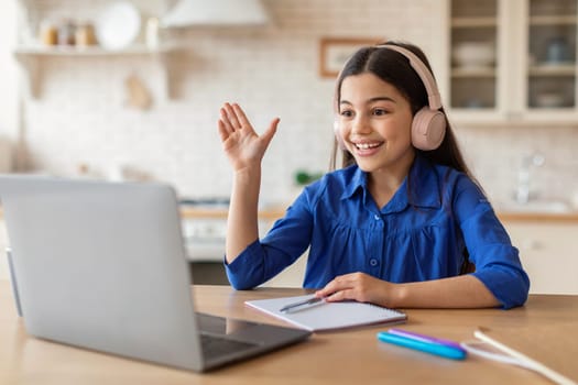 Schoolgirl With Headphones Raising Hand Learning Via Laptop At Home