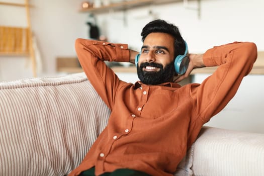 Cheerful indian man listening to music in headset at home
