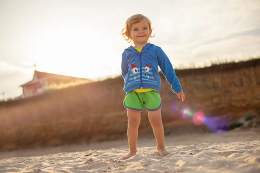 Happy child boy is walking on the beach at sunset. Cute blonde boy on a beach holiday.