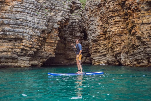 Young men Having Fun Stand Up Paddling in blue water seaamong the rocks in Montenegro. SUP