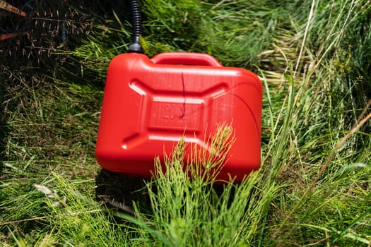 Red plastic canister among the green grass near the white car. Problems on the road with fuel for the car, refueling on the road, self-refueling.