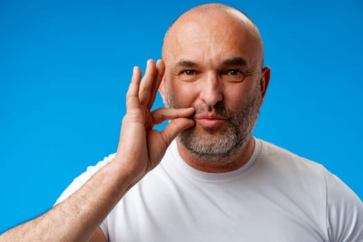 Middle age man wearing t-shirt over blue wall asking to be quiet