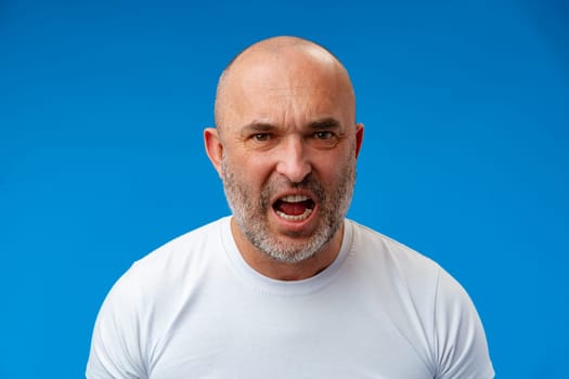 Frustrated bearded man shouting and screaming against blue wall