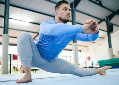 Sports, gymnastics and man stretching body ready to start training, exercise and workout in gym. Fitness, motivation and male athlete on floor with focus for balance, performance and competition