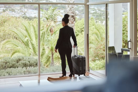 Travel, luggage and window with a business black woman standing in a hotel looking at the view. Corporate, glass and accommodation with a female employee in a luxury or modern apartment for work