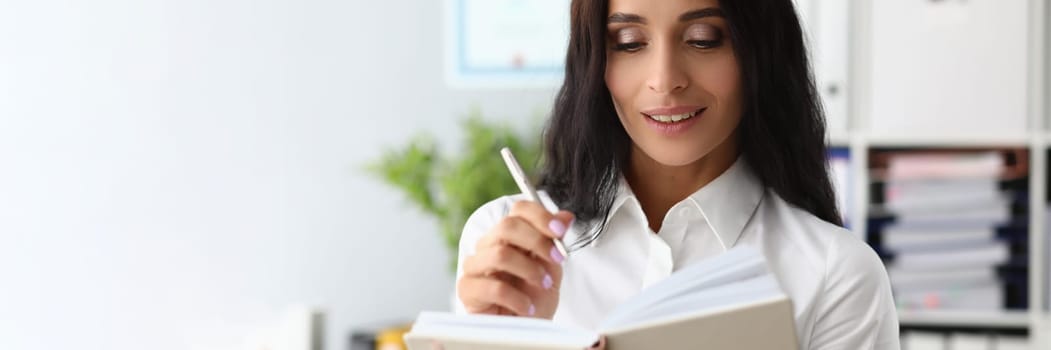Beautiful woman smiles thoughtfully and holds pen and diary