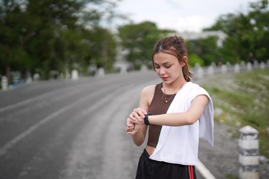 Young woman jogging and looking at her smart wrist watch, copy space, outdoor