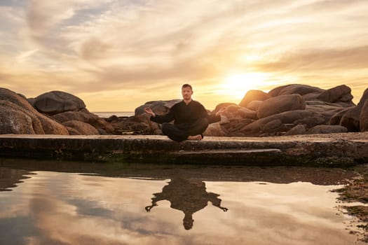 Sunset, yoga or zen man in meditation by a calm or peaceful lake or beach for a spiritual mindfulness exercise. Nature, wellness or healthy yogi in a lotus pose training his relaxed body to meditate