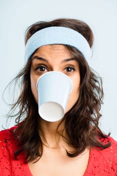 Thats my eighth cup today. a young woman standing in the studio and posing while wearing a headband and biting a coffee cup.