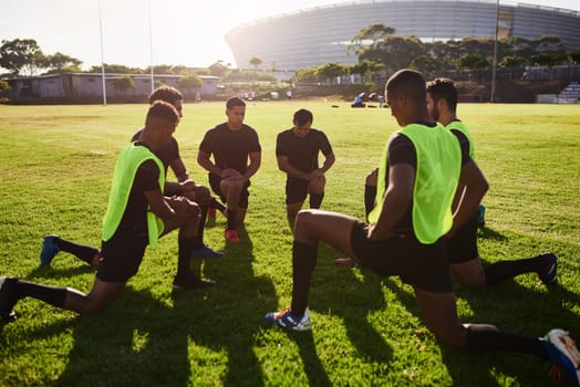 Making sure we dont have stiff muscles. Full length shot of a diverse group of sportsmen stretching before a rugby practice during the day.
