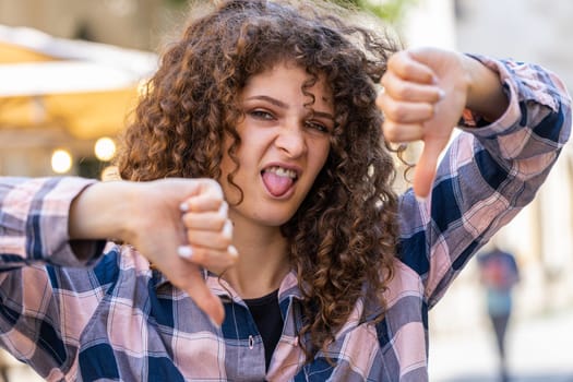 Dislike. Upset pretty young woman showing thumbs down sign gesture, expressing discontent, disapproval, dissatisfied bad work, mistake. Displeased girl walking in urban city sunshine street outdoors