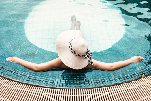 Sexy Woman in Swimsuit is Relaxing in Swimming Pool, Beautiful Woman Wearing Straw Hat and Relax Sunbathe in Poolside on Summer Holiday at Resort Hotel. Summer Vacation and Relaxation Lifestyles