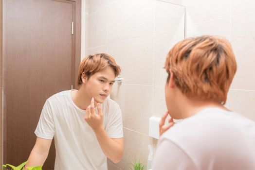 Reflection of young man in mirror checking his stubble in bathroom