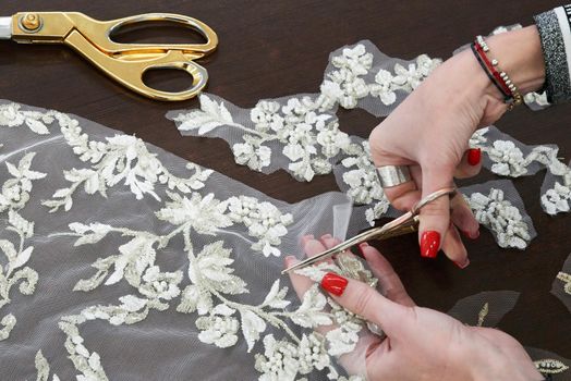 Dressmaker cutting lace fabric for wedding dress decoration