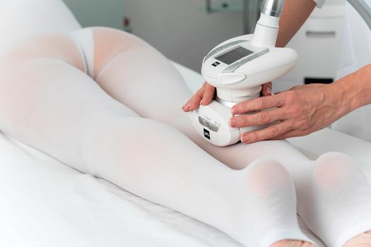 Woman in special white suit getting anti cellulite massage for legs in a spa salon. LPG, and body contouring treatment in clinic.