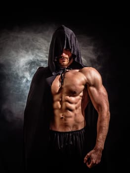 Scary muscular young man with pointed hood and cape