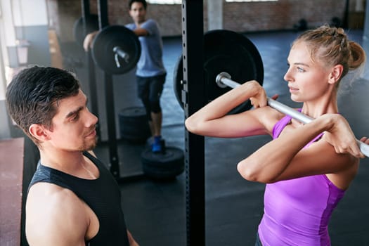 Set a goal and make it happen. a young woman lifting weights with her personal trainer assisting her.