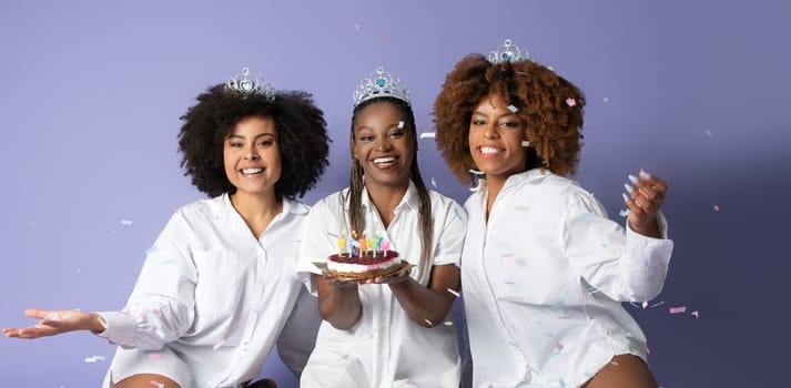 Black Ladies Holding Birthday Cake With Candles Over Purple Background