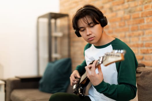 Chinese Guy Playing Electric Guitar with Earphones On At Home
