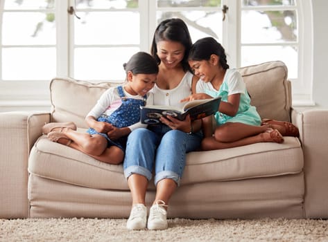 Females only reading a book together on the sofa at home and looking relaxed and happy while enjoying family time with their young mother