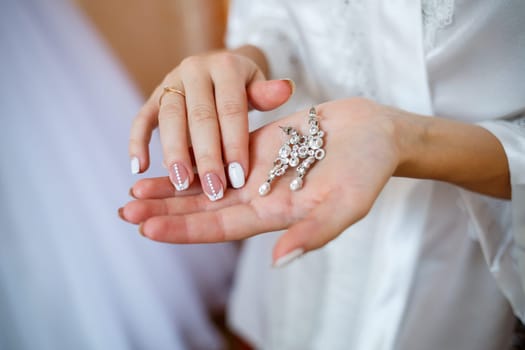 Beautiful wedding earrings in the hands of the bride on their wedding day
