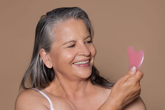 Portrait of happy european elderly woman with gray hair uses jade gouache petal