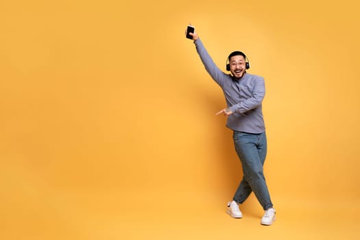 Crazy Fun. Cheerful Asian Man In Wireless Headphones Dancing On Yellow Background
