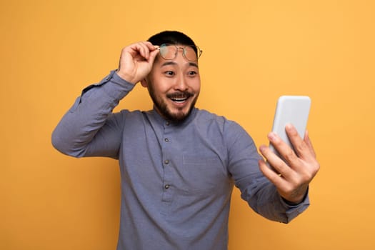 Portrait Of Amazed Asian Male Taking Off Glasses And Looking At Smartphone