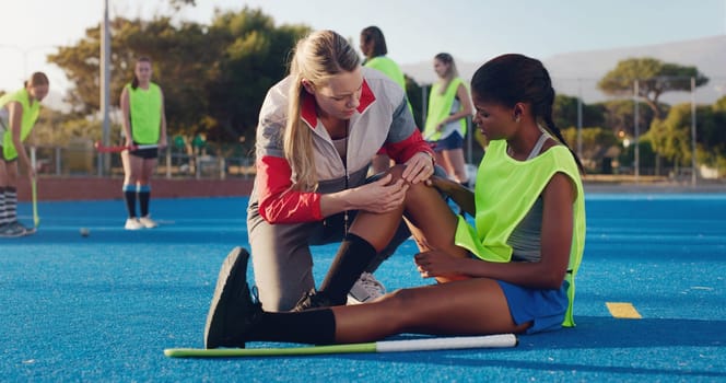 Woman, sports and knee injury in hockey training, practice or game on a blue turf with coach and team. Sport mentor helping female in leg pain, accident or bruise from physical activity during match