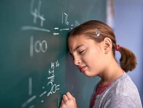She doesnt like not figuring it out. an elementary school girl pressing her head against the blackboard with frustration in class.