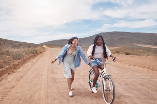 Bike ride, girl friends and road trip fun of women outdoor on a desert path on summer vacation. Cycling, running and freedom of young people together with bicycle transportation feeling free
