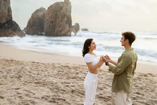Loving couple holding hands and looking at each other, having romantic date on the beach near ocean shore, free space.
