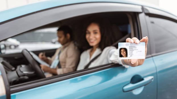 Happy middle eastern woman sitting in car showing driver license