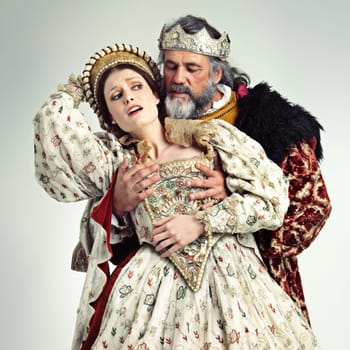 Theater, king and queen in costume with violence in in crown and renaissance clothes in studio. Art, cosplay and larp, couple in medieval play, royal history character and woman in distress with man.