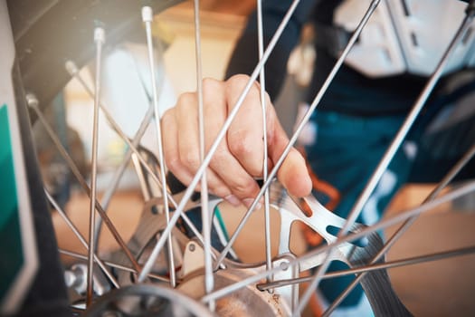 Motorcycle, wheel and hands on spokes with a man at work in a repair shop or maintenance garage. Bike, mechanic and service with a professional handyman working on a bicycle rim in a workshop