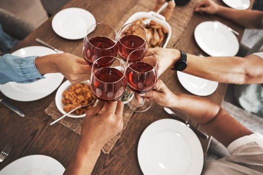Top view, hands and toast with red wine at dinner table for new year celebration in home. Party, cheers and group of friends, men and woman with alcohol or beverage to celebrate with delicious food.