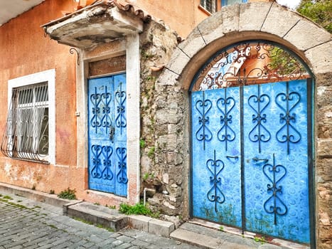 Facade of old village house with blue door and gate with patterned forging